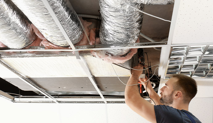 Technician repairing air ducts and wiring in suspended ceiling