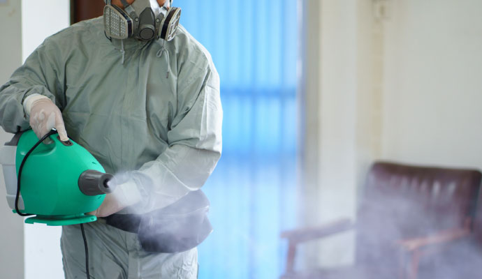 Person in protective suit operating fogging device for smoke odor removal