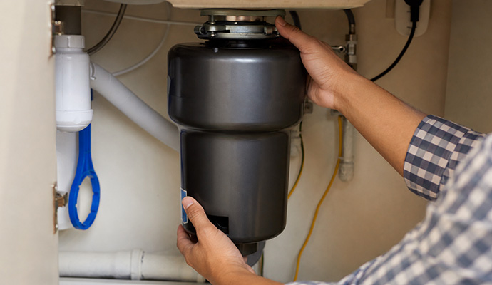 Technician replacing garbage disposal unit under kitchen sink
