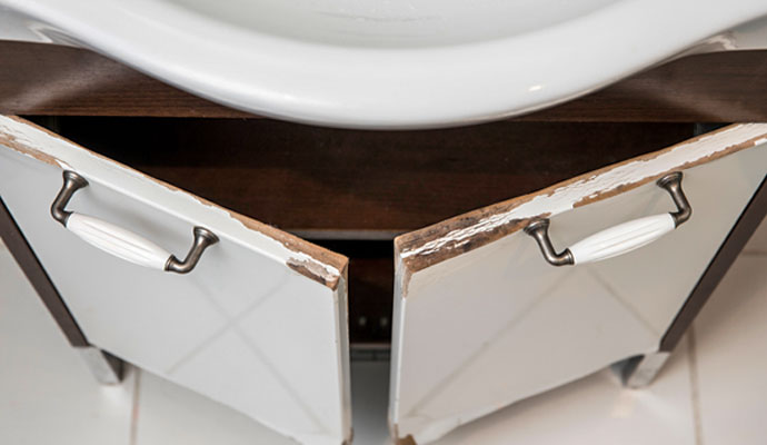 Water damaged cabinet doors with peeling paint under sink